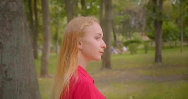 Primer plano vista lateral retrato de la joven rubia de pelo largo hermosa hembra caminando en el parque al aire libre — Vídeos de Stock