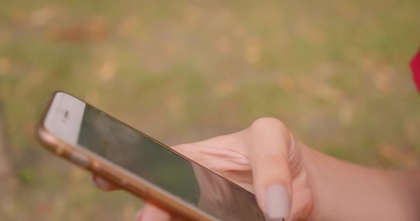 屋外の公園で携帯電話を保持する若い白人女性の手のクローズアップ肖像画 — ストック動画