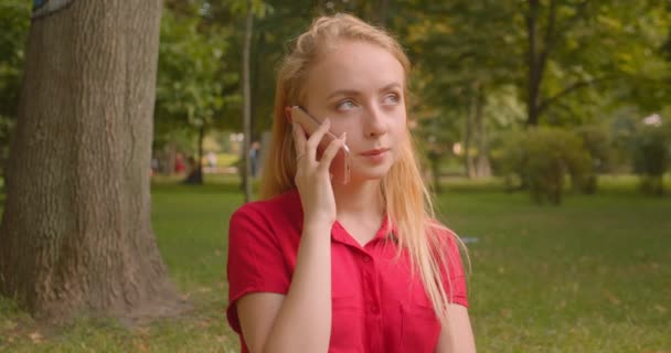 Primer plano retrato de la joven rubia de pelo largo hermosa hembra teniendo llamada telefónica en el parque al aire libre — Vídeos de Stock