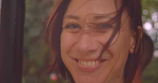 Крупним планом портрет молодої кавказької жінки дивиться на камеру, що посміхається щасливо, поки йде дощ у міському місті на відкритому повітрі — стокове відео