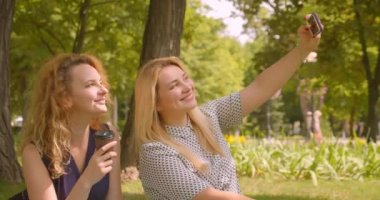 Park açık havada battaniye üzerinde oturan telefonda selfie çeken iki kadın arkadaşın yakın çekim portresi
