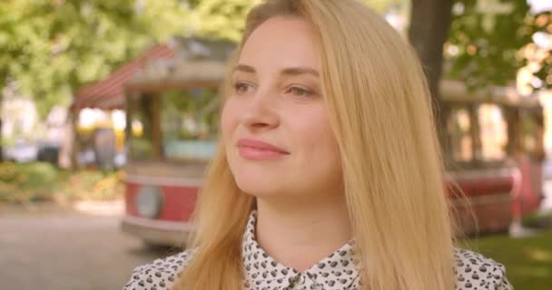 Closeup portrait of adult blonde female holding coffee looking at camera smiling cheerfully in park outdoors — Stock Video