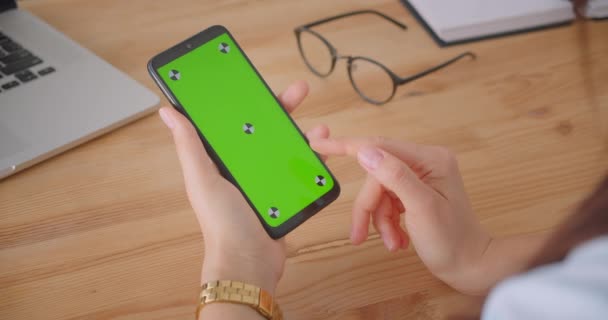 オフィス内の緑のクロマキー画面と携帯電話を使用して若い女性医師の手のクローズアップバックビューの肖像画 — ストック動画