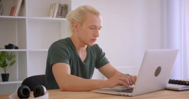 Ofiste kamera kapalı bakarak dizüstü bilgisayar kullanarak genç sarışın hipster işadamı Closeup portre