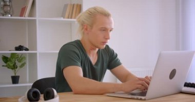 Ofiste kamera kapalı bakarak dizüstü bilgisayarda yazarak genç sarışın hipster işadamı Closeup portre