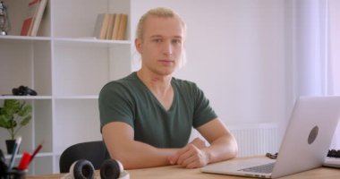 Genç sarışın hipster işadamının dizüstü bilgisayarda yazarak ofis içinde düşünceli olan kameraya bakarak yakın çekim portresi