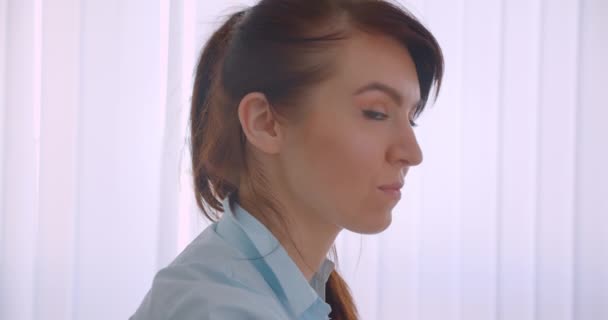 Closeup oldalnézetből portréja fiatal sikeres vonzó kaukázusi női orvos nézi kamera beltéri hivatalban — Stock videók