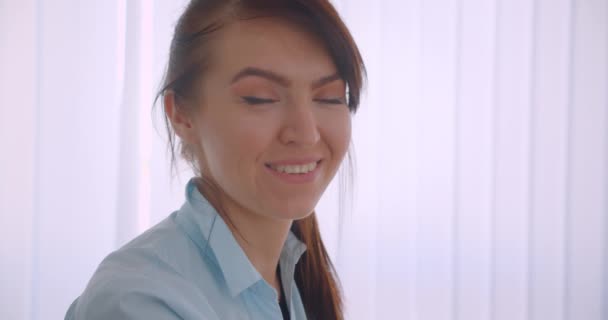 Primer plano vista lateral retrato de joven exitoso atractivo caucásico médico femenino en abrigo mirando a la cámara sonriendo alegremente en el interior de la oficina — Vídeo de stock