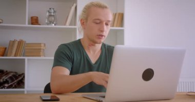 Genç yakışıklı sarışın hipster işadamının dizüstü bilgisayarda gezinme ve ofiste kapalı telefon üzücü bildirim alma Closeup portre