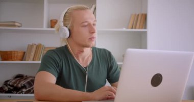 Ofiste dizüstü bilgisayar kullanarak kulaklık genç yakışıklı sarışın hipster işadamıCloseup portre