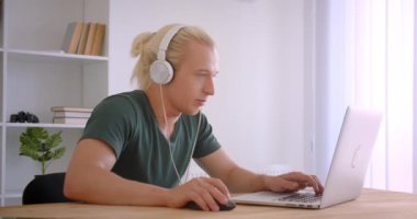 Ofiste kapalı mekanlarda müzik dinleyerek dizüstü bilgisayar kullanan kulaklıkgenç yakışıklı sarışın hipster işadamının Closeup portresi