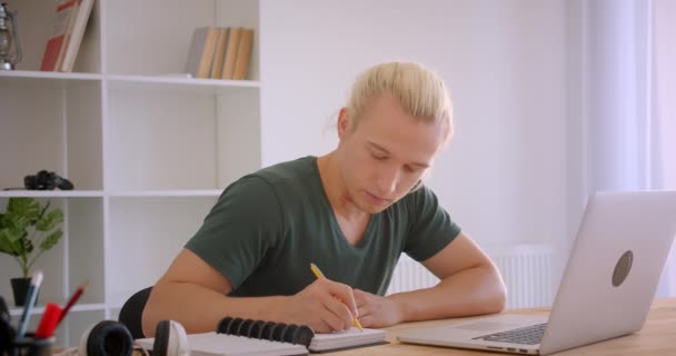 Primer plano retrato de joven atractiva rubia hipster hombre de negocios utilizando el ordenador portátil tomando notas en el interior de la oficina — Vídeos de Stock