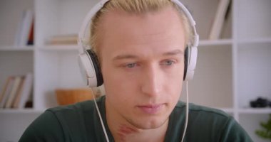 Kulaklık genç çekici sarışın hipster adam closeup portre kamera neşeyle kapalı gülümseyerek bakarak