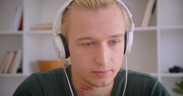 Closeup portrét mladého přitažlivého blonďáku ve sluchátkách s veselým úsměvem v interiérech — Stock video