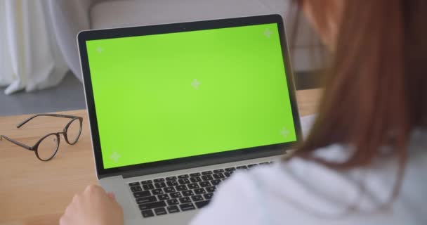 オフィスの屋内で緑色のクロマスクリーンを持つラップトップを使用して若い白人女性医師のクローズアップバックビューの肖像画 — ストック動画