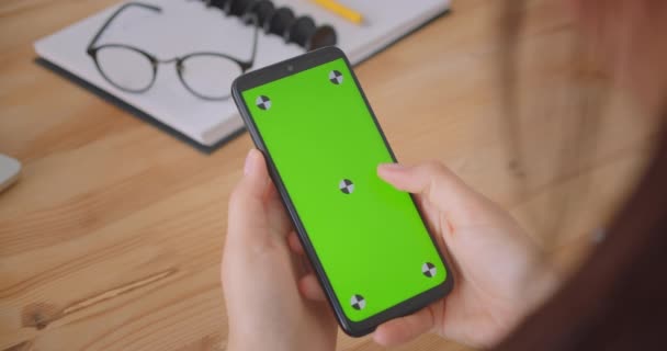 Closeup back view portrait of young female hand texting on phone with green chroma key screen indoors in office — Stock Video