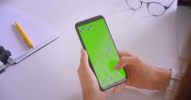 Genç güzel beyaz iş kadınlarının kapalı ofis içinde yeşil ekranlı el tutan telefonun closeup portresi