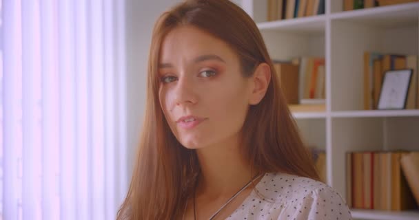 Портрет крупным планом молодой кавказской предпринимательницы, счастливо смотрящей на камеру в библиотеке с книжными полками на заднем плане — стоковое видео