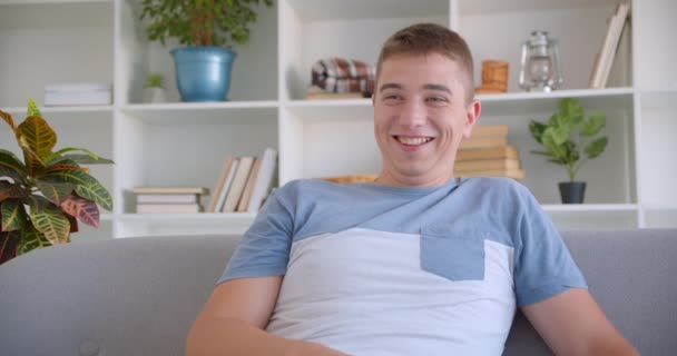 Closeup retrato de adulto atraente caucasiano homem assistindo TV rindo alegremente segurando controle remoto sentado no sofá dentro de casa — Vídeo de Stock