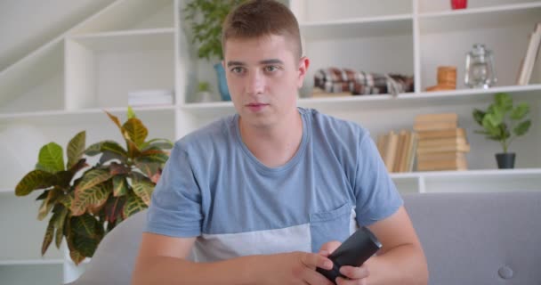 Primer plano retrato de hombre caucásico atractivo adulto viendo esportrs en la televisión y celebrando la celebración de control remoto sentado en el sofá interior — Vídeos de Stock