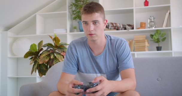 Primer plano retrato de adulto atractivo caucásico hombre jugando videojuegos sentado en el sofá en interiores — Vídeos de Stock