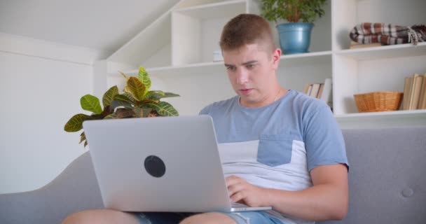 Zbliżenie portret dorosłych atrakcyjny kaukaski mężczyzna za pomocą laptopa patrząc na aparat uśmiechnięty szczęśliwie siedzi na kanapie w pomieszczeniu — Wideo stockowe