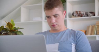 Arka kamera yada kanepede otururken gülümseyen kameraya bakan dizüstü bilgisayar kullanan yetişkin çekici beyaz adamın closeup portresi