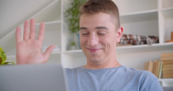 Gros plan portrait de l'homme caucasien attrayant adulte ayant appel vidéo sur ordinateur portable saluant salut assis sur le canapé à l'intérieur — Video