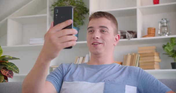 Nahaufnahme Portrait von erwachsenen attraktiven kaukasischen Mann mit Videoanruf am Telefon sitzen auf der Couch drinnen — Stockvideo