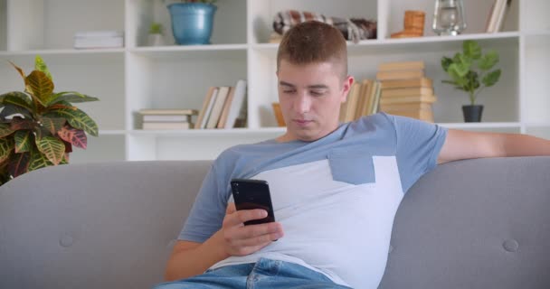 Nahaufnahme Porträt eines erwachsenen attraktiven kaukasischen Mannes, der auf dem Sofa im Haus sitzt und SMS schreibt — Stockvideo