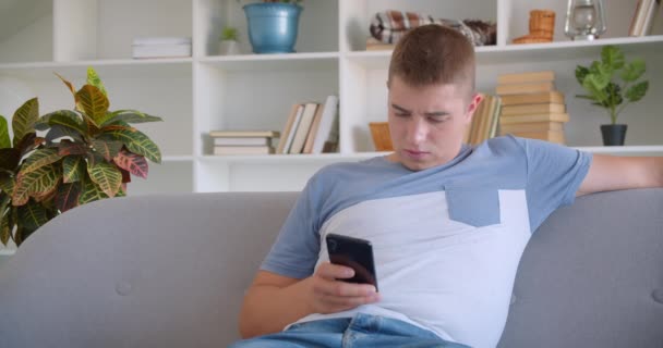 Closeup retrato de adulto atraente caucasiano homem usando telefone sentado no sofá dentro de casa — Vídeo de Stock