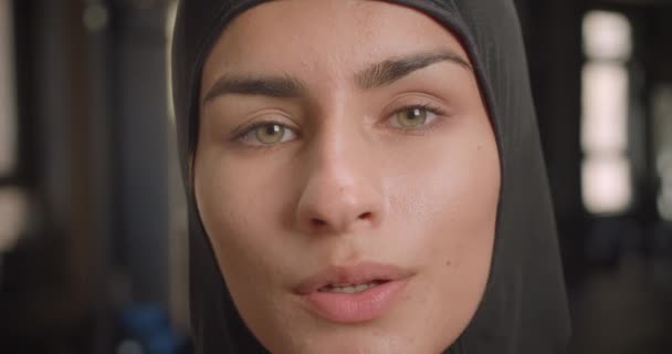 Close-up portret van jonge succesvolle atletische moslim vrouw kijken naar camera met vastberadenheid staande in de sportschool binnenshuis — Stockvideo