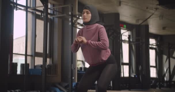 Close-up portret van jonge aantrekkelijke atletische moslim vrouwelijke maken squats in de sportschool binnenshuis — Stockvideo