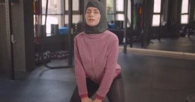 Genç kararlı atletik müslüman kadın kapalı spor salonunda dambıl ile squats yapma Closeup portre