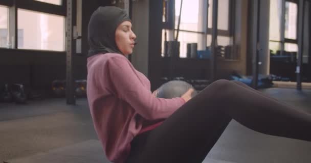 屋内のジムでボールを使って運動するヒジャーブの若い運動運動教徒の女性のクローズアップ肖像画 — ストック動画