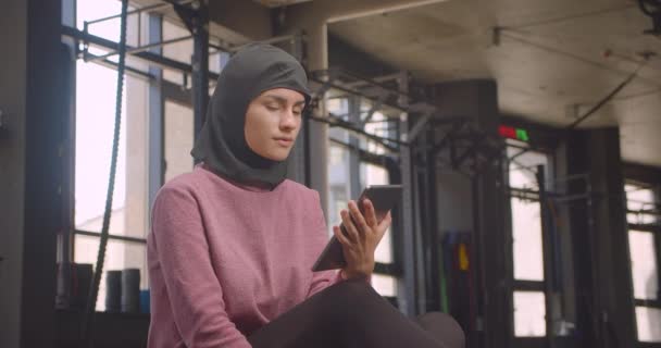 Retrato de primer plano de una joven atlética musulmana en hijab usando tableta y mostrando la pantalla de croma verde a la cámara en el gimnasio en interiores — Vídeos de Stock