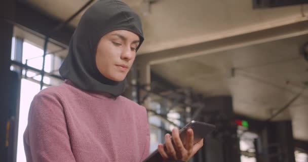 태블릿을 사용하여 히잡에서 젊은 운동 무슬림 여성의 클로즈업 초상화 와 실내 체육관에서 카메라에 녹색 크로마 키 화면을 보여주는 — 비디오