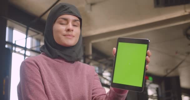 Closeup portrét mladé atletické samice v hidžábu pomocí tabletu a zobrazující zelenou obrazovku Chroma s klíčem na kameru v tělocvičně v interiérech — Stock video
