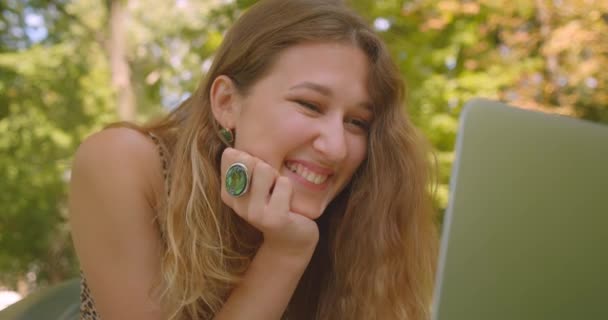 Close-up portret van jonge mooie blanke vrouw met een video-oproep op laptop praten gelukkig leggen op tapijt op gras in Park — Stockvideo