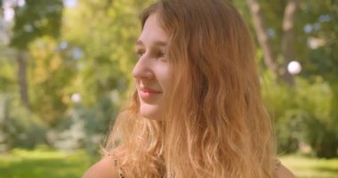 Park açık havada mutlu bir şekilde gülümseyen kameraya bakan genç, beyaz beyaz bir kadının yakın çekim portresi