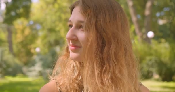 Крупный план портрета молодой белой девушки, счастливо улыбающейся в парке — стоковое видео
