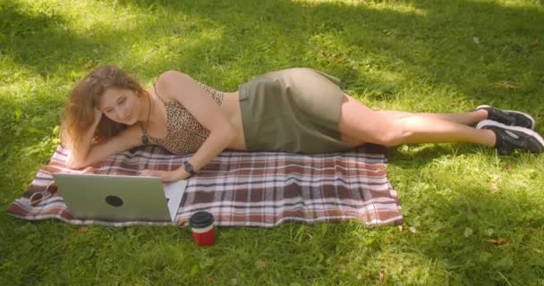 Primo piano ritratto di giovane bella femmina caucasica sdraiata su un tappeto utilizzando il computer portatile sorridente felicemente nel parco all'aperto — Video Stock