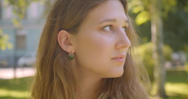 Closeup portrait of young pretty caucasian female looking at camera smiling cheerfully standing in park outdoors — Stock Video