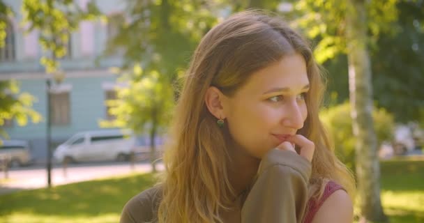Närbild porträtt av unga söta kaukasiska kvinna tittar på kamera leende lyckligt stående i parken utomhus — Stockvideo