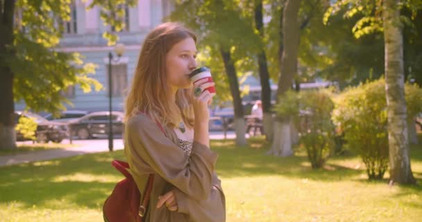 Gros plan côté vue portrait de jeune mignon caucasien femelle regardant caméra boire café souriant heureux debout dans le parc à l'extérieur — Video