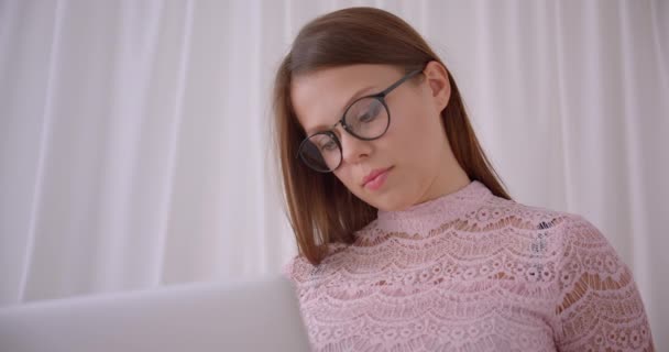 Closeup retrato de jovem atraente mulher de negócios caucasiana usando laptop olhando para a câmera sorrindo alegremente sentado no sofá dentro de casa — Vídeo de Stock