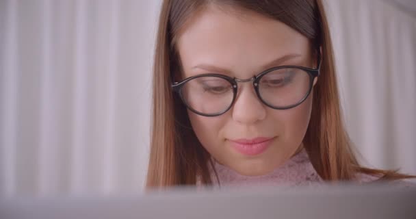 Портрет крупным планом молодой привлекательной кавказской предпринимательницы в очках, печатающей на ноутбуке в помещении квартиры — стоковое видео
