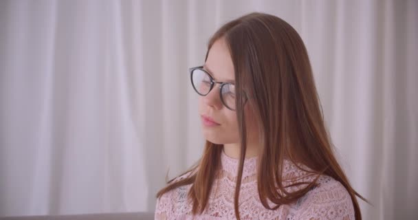 Gros plan portrait de jeune jolie femme caucasienne dans des lunettes regardant la caméra souriant joyeusement à l'intérieur dans l'appartement — Video