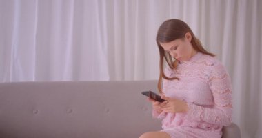 Genç çekici beyaz kadın telefonda mesajlaşma Closeup portre daire içinde kanepede otururken neşeyle gülüyor