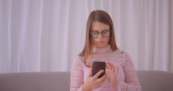 Close-up portret van jonge aantrekkelijke blanke vrouw met behulp van telefoon en het tonen van groen scherm naar camera zittend op de Bank binnenshuis in appartement — Stockvideo